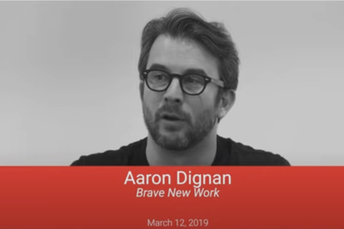 A black-and-white image of Aaron Dignan, author of "Brave New Work," speaking. The red text overlay at the bottom displays his name, the book title, and the date "March 12, 2019."